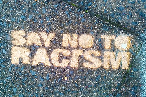 Es ist ein Bild der gesprühten Parole "Say no to racism" auf Gehwegplatten zu sehen.